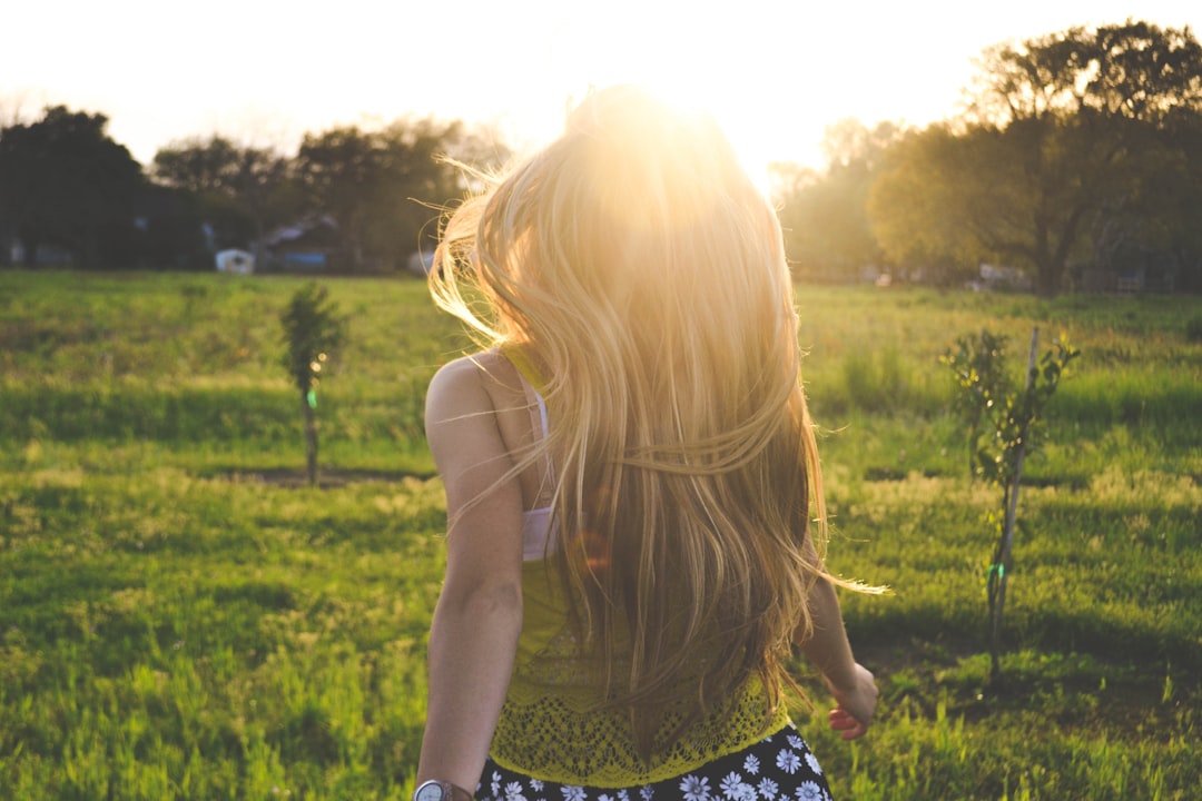 Sunlight welcomes blonde girl by Makeup Brands woman walking on lawn with trees